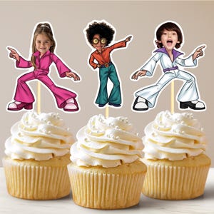 May include: Three cupcakes decorated with images of people dressed in 1970s disco attire. The cupcakes are white with white frosting and white sprinkles.