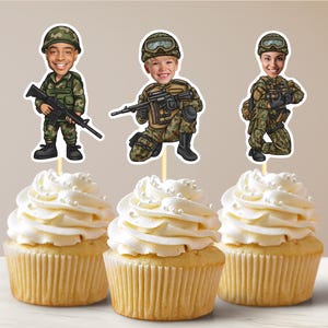 Könnte beinhalten: Drei Cupcakes, die mit militärischen Toppern verziert sind. Die Topper zeigen Comicbilder von Personen in Tarnuniformen, die Gewehre halten.