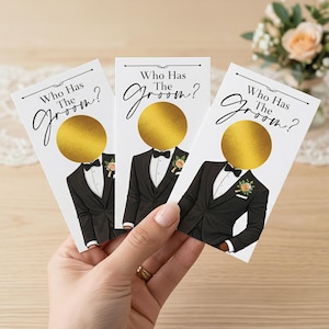 May include: Three white cards with the text "Who Has The Groom?" and a graphic of a man in a black tuxedo with a gold circle for a face. The cards are held in a hand.