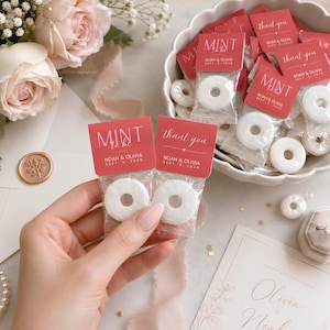May include: Two small clear plastic bags containing white ring-shaped mints, each topped with a coral-coloured card. One card reads MINT to be NOAH & OLIVIA SEPT. 5, 2026, and the other reads thank you NOAH & OLIVIA SEPT. 5, 2026 in white text.