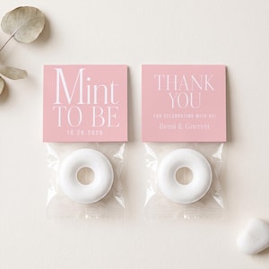 May include: Two square pink paper toppers attached to clear plastic bags containing white ring-shaped mints. The left topper reads Mint To Be 10.26.2026. The right topper reads Thank You For Celebrating With Us! Remi & Garrett in white text.