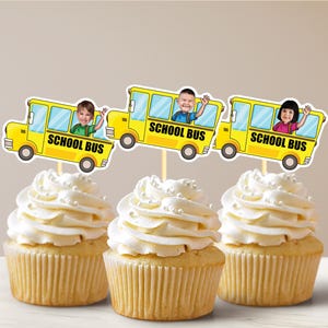 May include: Three yellow school bus cupcake toppers with personalized photos of children. Each topper features the words "School Bus" and a yellow school bus with a smiling child inside. The toppers are placed on top of cupcakes with white frosting.