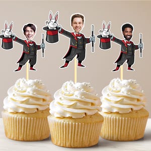 May include: Three cupcakes with white frosting and pearl sprinkles. Each cupcake is topped with a magician-themed cutout. The cutouts feature a cartoon magician holding a wand and a rabbit in a hat.