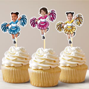 May include: Three cupcakes with white icing and sprinkles topped with personalised cheerleading cupcake toppers. Each topper features a person with a different coloured cheerleading outfit and pom-poms.