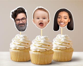 Puede incluir: Tres cupcakes con glaseado blanco y chispas de perlas, cada uno coronado con un recorte de cara diferente. Las caras son de un hombre con barba, un bebé y una mujer.