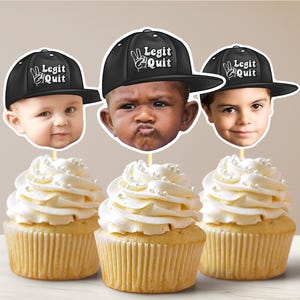 May include: Three cupcakes decorated with white frosting and white sprinkles. Each cupcake has a black and white paper topper with a person's face and a black baseball cap with the text "Legit Quit" on it.