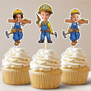 Op de afbeelding: Drie cupcakes versierd met bouwvakker-toppers. Elke topper toont een cartoonfiguur met een gele helm en een blauwe overall. De cupcakes zijn bedekt met witte frosting en hebben witte sprinkles.