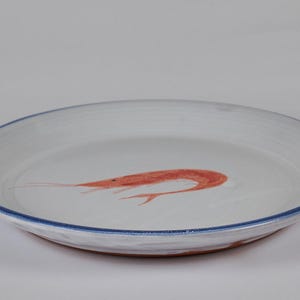 Könnte beinhalten: Weißer Keramikteller mit blauem Rand und einem handgemalten orangefarbenen Garnelen-Design in der Mitte. Der Teller hat einen leicht erhöhten Rand und ein rustikales, handgefertigtes Aussehen, ideal zum Servieren von Meeresfrüchten.