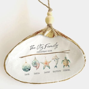 May include: A white seashell ornament with gold trim, featuring the text "The Utz Family Christmas 2024". Five ornaments hang from a branch, each with a name and a sea-themed design.