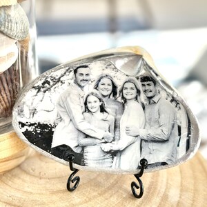May include: A black and white photo of a family of five is printed on a white seashell. The seashell is on a black metal stand.