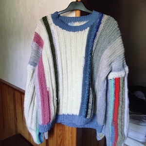 Peut inclure: Un pull en crochet rayé blanc, bleu, rose et vert avec un col bleu.