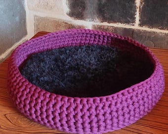 May include: A purple crocheted pet bed with a black fleece lining.