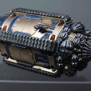May include: A detailed miniature model of a futuristic vehicle, featuring a metallic gold and blue color scheme. The model has a complex design with intricate details, including a track system, multiple turrets, and a drill-like front. The overall aesthetic suggests a science fiction or fantasy theme.
