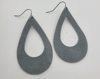 May include: A pair of gray suede teardrop earrings with a cutout design. The earrings have silver hooks.