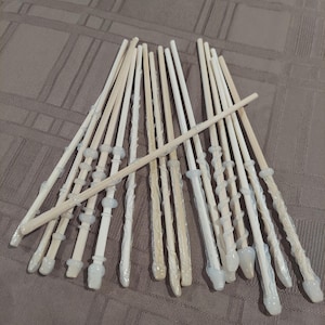 May include: A collection of light-colored wands with various designs. Some wands have decorative handles and tips, while others have a smooth, simple design. The wands are made of wood and have a magical theme.