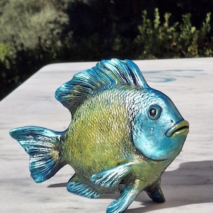 Op de afbeelding: Een decoratief visbeeldje met een metallic afwerking met een verloop van iriserend blauw op de kop en vinnen, overgaand in een getextureerd, glinsterend limoengroen lichaam. De vis heeft een ronde vorm, opvallende schubben en donkere ogen.