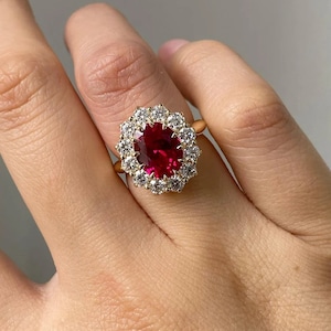 May include: A gold ring featuring a large oval ruby surrounded by a halo of smaller diamonds.