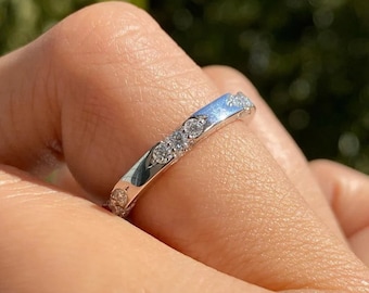May include: A thin silver band with small round diamonds set in a pave setting.