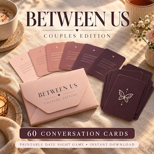 Op de afbeelding: Een kaartspelset getiteld BETWEEN US COUPLES EDITION met een lichtroze doos in envelopstijl en een stapel van 60 gesprekskaarten in roze en donkerpaarse tinten. De kaarten tonen een vlinderillustratie en tekstlijnen om op te schrijven.