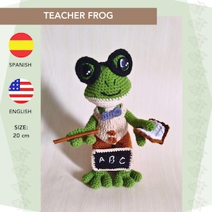 May include: A handmade green crochet frog wearing glasses, a bow tie, and a vest. The frog holds a pointer and a small chalkboard with "ABC" written on it. The frog is approximately 8 inches tall.