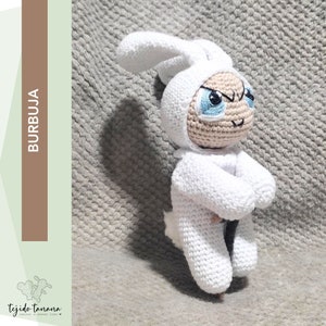 Puede incluir: Juguete de conejo blanco de crochet con ojos azules. El conejo lleva un atuendo de crochet blanco y tiene una expresión de enfado.