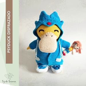 Puede incluir: Un juguete de peluche Psyduck tejido a crochet con una chaqueta azul con capucha y sosteniendo una muñeca de crochet más pequeña. El peluche Psyduck tiene un cuerpo amarillo, un pico marrón y un punto rojo en la cabeza.