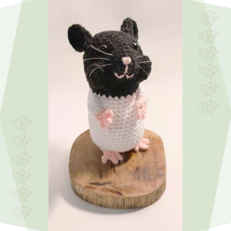 May include: A crocheted black and white hamster wearing a white crocheted shirt. The hamster is standing on a wooden base.