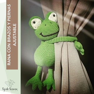 May include: Green crocheted frog curtain tieback with white eyes. The frog is holding onto a beige curtain with its arms and legs.