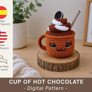 Op de afbeelding: Een gehaakte kop warme chocolademelk, ongeveer 10 cm hoog, met een lachend gezicht, slagroom en een Oreo. De bruine beker heeft een oor en staat op een houten schijf. De tekst "CUP OF HOT CHOCOLATE - Digital Pattern" is zichtbaar.