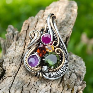 May include: A silver and gold pendant with a cluster of five gemstones. The gemstones are a pink ruby, an orange garnet, a yellow citrine, a purple amethyst, and a green peridot.
