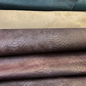 May include: Close-up of four different pieces of faux leather fabric. The fabric has a snakeskin pattern and is in shades of teal, beige, dark purple, and light purple.