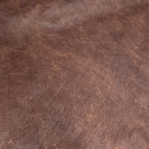 May include: Close-up of a brown leather texture with a slightly distressed look. The leather has a natural grain pattern and a subtle sheen.
