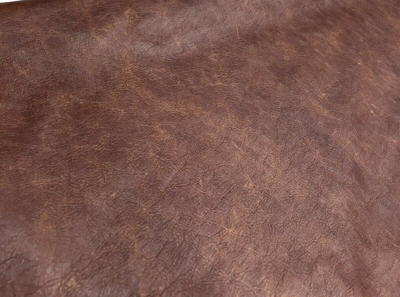 May include: Close-up of a brown leather texture with a slightly distressed look. The leather has a natural grain pattern and a subtle sheen.
