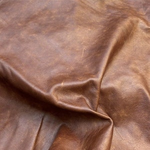 May include: Close-up of a brown leather surface with a wrinkled texture. The leather has a worn, vintage look.