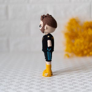 May include: A crocheted figurine of a person wearing a black and blue jersey with a yellow star on the chest, black shorts with blue stripes, and yellow shoes.