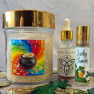 以下が含まれることがあります： 金色の蓋が付いたガラス瓶に、バスソルトが入っています。ラベルには「Magical Pot of Gold Bath Salts」と書いてあり、虹と金の壺が描かれています。瓶の隣には、エッセンシャルオイルのボトルが2本あります。1本のボトルには「Golden Skin Serum」と書いてあり、緑のクローバーと蝶が描かれています。もう1本のボトルには「Lucky Charm」と書いてあり、緑のクローバーと金貨が描かれています。