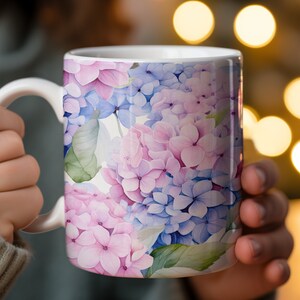 May include: White ceramic mug with a floral design featuring pink and blue hydrangeas. The mug has a handle and is perfect for enjoying a hot beverage.