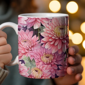May include: A white ceramic mug with a pink floral design. The mug features a close-up of pink chrysanthemums with green leaves.