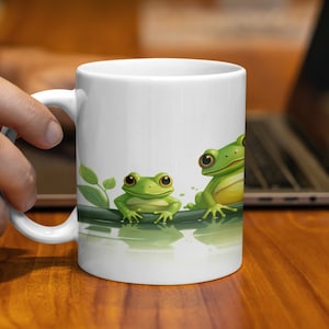 May include: White ceramic mug with a design of three green frogs sitting on a branch. The frogs are facing different directions and have black eyes.