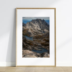 May include: A framed photograph of a mountain range with two lakes in the foreground. The mountains are rocky and jagged, and the lakes are a deep blue. The photo is taken from a high vantage point, and the sky is a light blue.