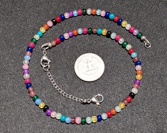 May include: A colorful beaded necklace with a silver clasp and extension chain. The necklace features small, round beads in various colors, including red, blue, green, yellow, and purple. A quarter coin is next to the necklace.