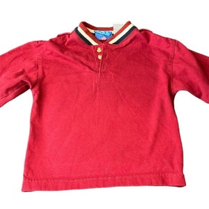May include: Red long-sleeve shirt with navy blue and white trim on the sleeves. The shirt has a button-up collar and a small patch on one sleeve that says "B.I.G.S."