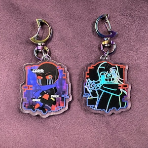 Peut inclure: Deux porte-clés en acrylique irisé représentant un personnage noir et bleu avec une écharpe rouge et bleue. Le personnage est intitulé "Error".