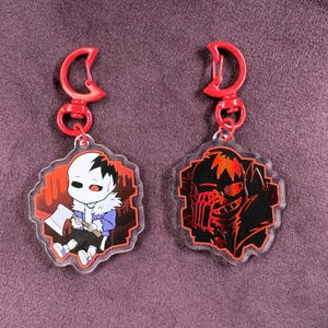 May include: Two red and black acrylic keychains featuring a cartoon character with a red axe and a red and black character with a red eye.