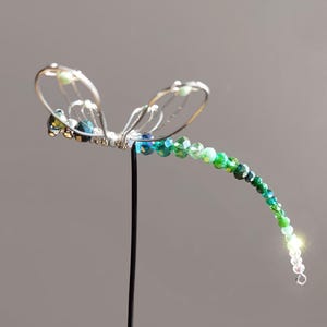 Könnte beinhalten: Eine Libelle aus Silberdraht mit einem Schwanz aus grünen und blauen Kristallperlen.