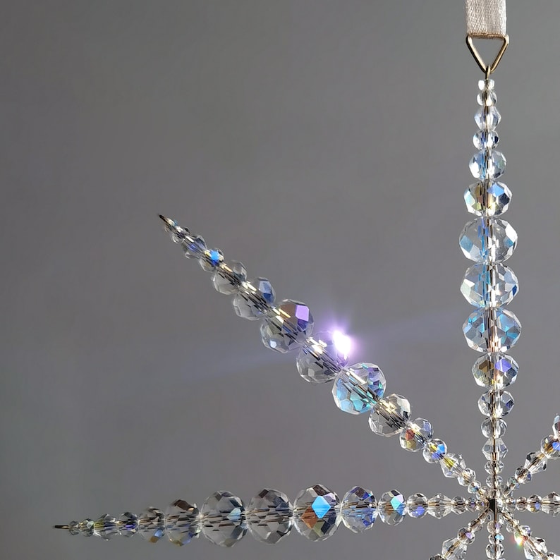 Makroaufnahme eines Fensterhänger Sterns aus glitzernden Kristallperlen. Die Sonnenstrahlen bringen den Kristallstern zum Funkeln, wie einen Sonnenfänger.