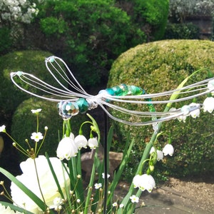 Pflanzstecker-Libelle auf Steckstab steckt zur Zierde in einem Blumen bouquet.
Im Hintergrund sieht man den Garten.