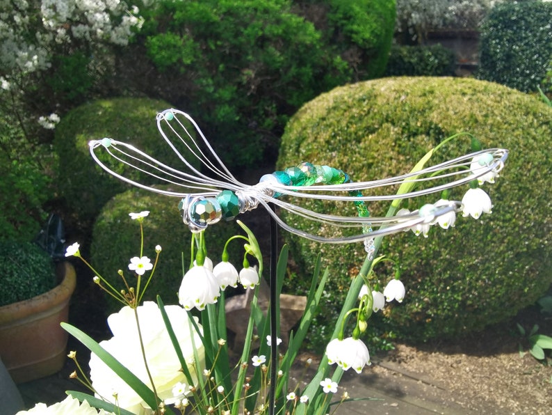 Pflanzstecker-Libelle auf Steckstab steckt zur Zierde in einem Blumen bouquet.
Im Hintergrund sieht man den Garten.