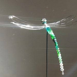 Libellen Gartenstecker aus grünen, facettierten Rondell-Perlen aus Glas vor grauem Hintergrund. Die Flügel sind aus Draht geformt.
Die Perlenfunkeln stark in der Sonne.
