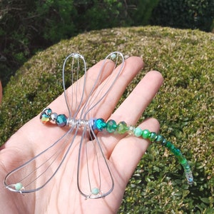 Drahtlibelle aus grünen Kristallperlen liegt auf einer Hand. Die Perlen glitzern in der Sonne.
